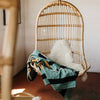 Wicker hanging chair with a blanket and pillow on a wooden floor.