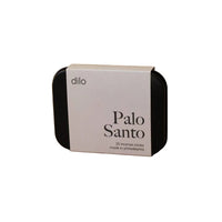 A rectangular black tin with rounded corners and a white paper band label reading 'dilo Palo Santo 25 incense cones made in philadelphia,' photographed on a plain warm beige background.