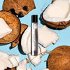 Perfume bottle labeled 'Dirty Coconut' surrounded by coconut halves on a blue background