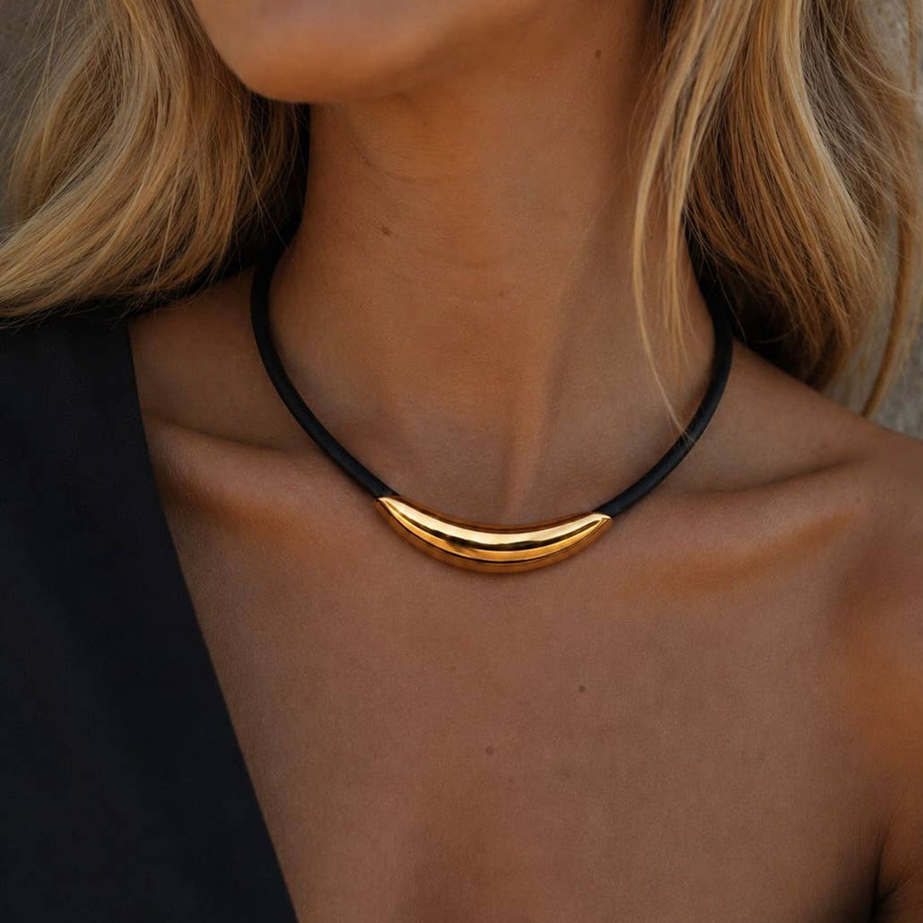 A close-up of a model wearing a black cord necklace with a polished gold crescent-shaped pendant.