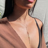 Close-up of a person wearing a delicate gold necklace with a neutral background