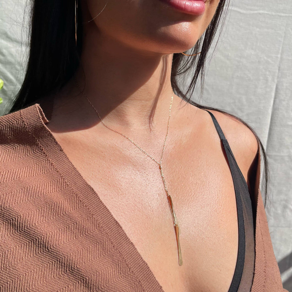 Close-up of a person wearing a delicate gold necklace with a neutral background