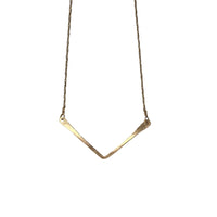 Gold necklace with a V-shaped pendant on a textured stone surface