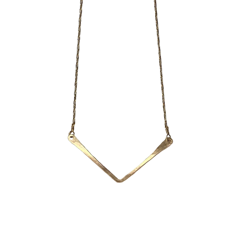 Gold necklace with a V-shaped pendant on a textured stone surface