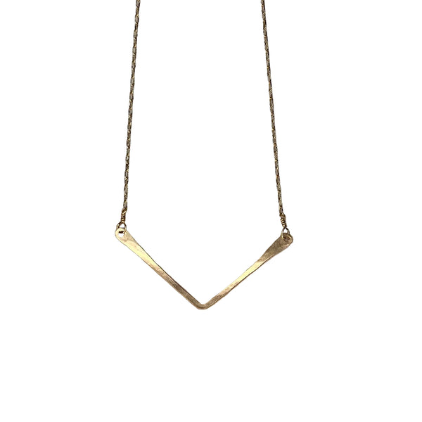 Gold necklace with a V-shaped pendant on a textured stone surface
