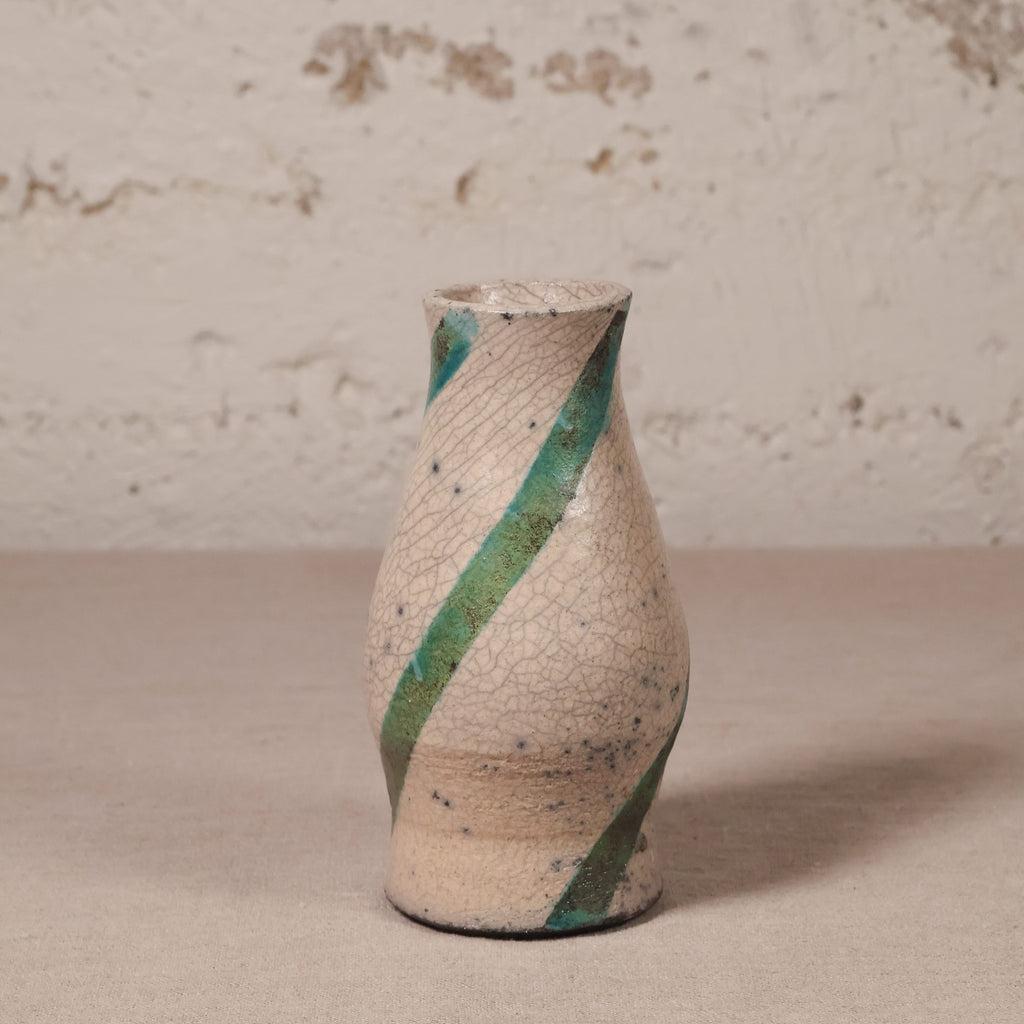 Ceramic vase with green stripe on a beige surface and textured wall background