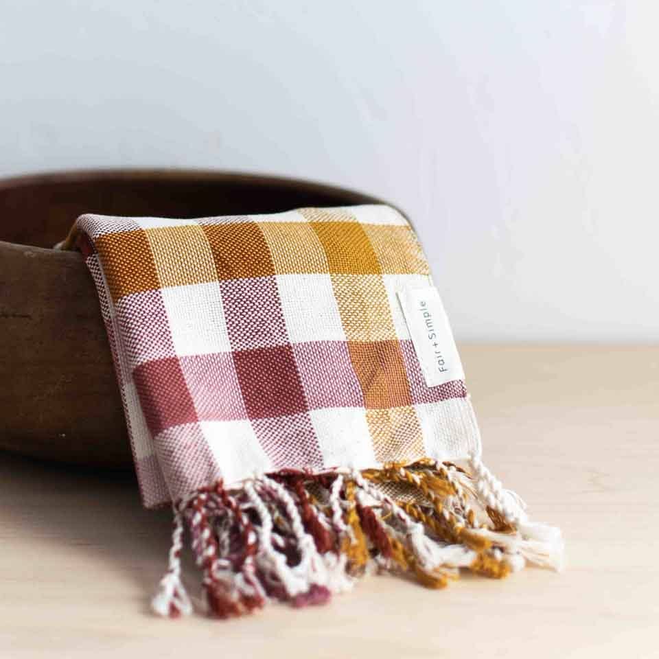 Plaid blanket with fringes draped over a wooden bowl on a light surface.
