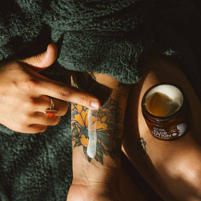 Person applying a product to their arm with a jar of lotion nearby, wrapped in a dark towel.