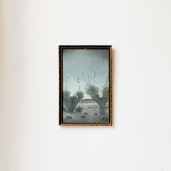 Framed artwork of a desert landscape with cacti on a white wall