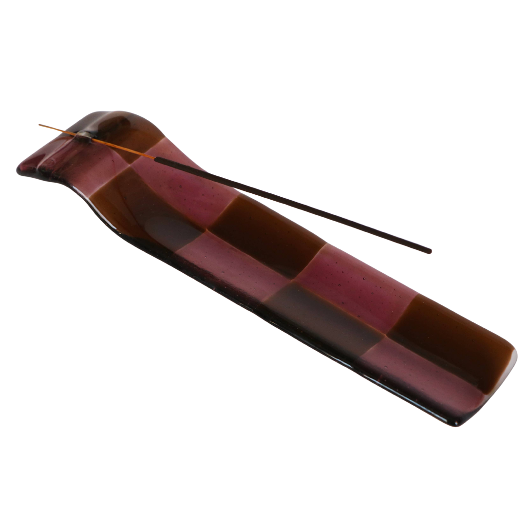A glossy rectangular incense holder with a checkered pattern of dark brown and deep burgundy, featuring a thin incense stick resting across it, set against a plain white background.