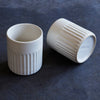 Two white ceramic containers with ribbed texture on a dark blue background
