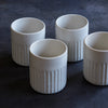 Four white ceramic cups with ribbed texture on a dark background