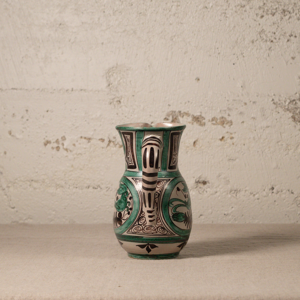 Decorative ceramic pitcher with green and black patterns on a textured surface.