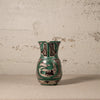 Ceramic pitcher with green and black floral patterns on a textured surface.
