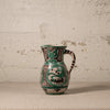 Ceramic pitcher with green and black patterns on a textured surface