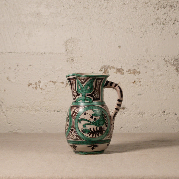 Ceramic pitcher with green and black patterns on a textured surface
