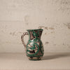 Ceramic pitcher with green and black patterns on a textured surface