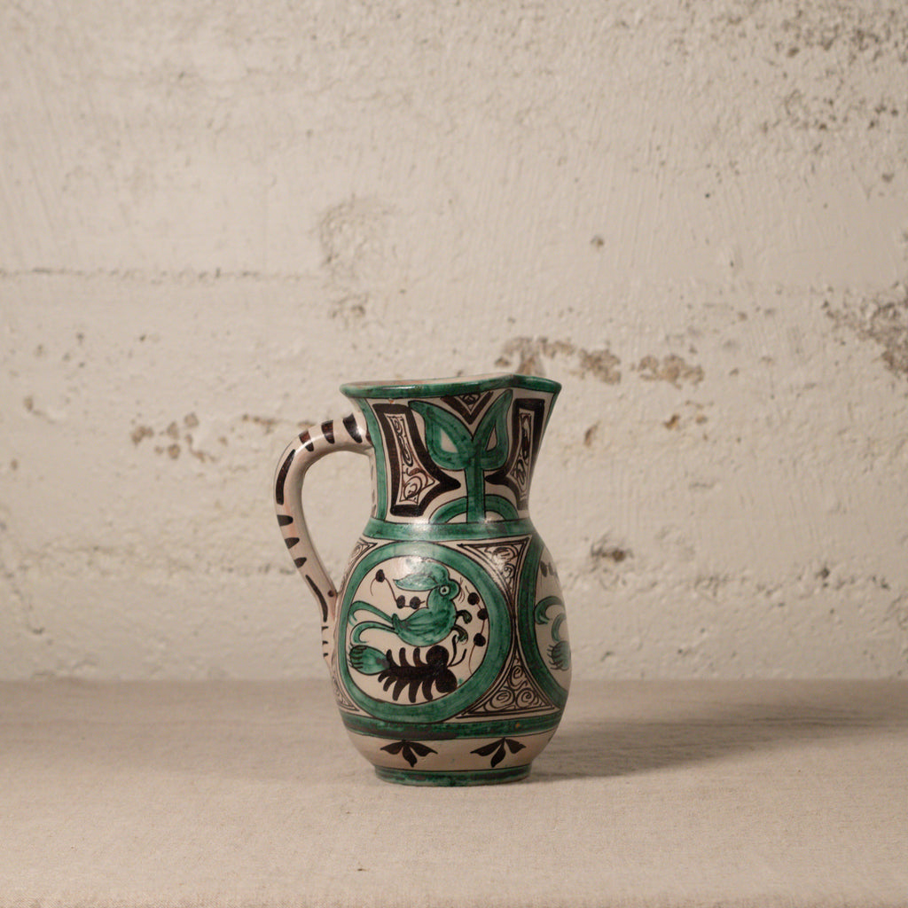 Ceramic pitcher with green and black patterns on a textured surface