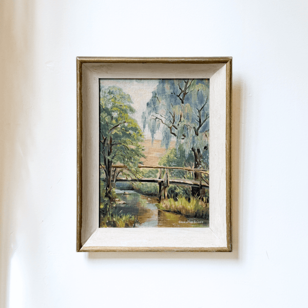 Framed painting of a bridge over a stream with trees on a white wall