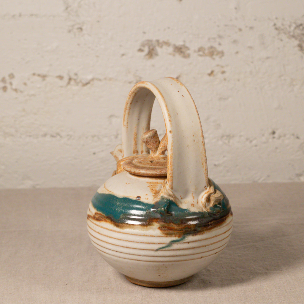 Ceramic teapot with decorative handles on a textured surface