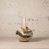 Vintage ceramic teapot with brown and green glaze on a textured surface.