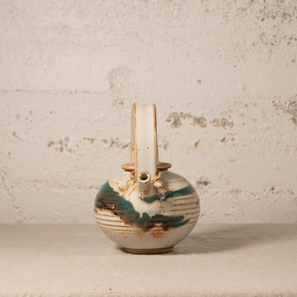 Vintage ceramic teapot with brown and green glaze on a textured surface.