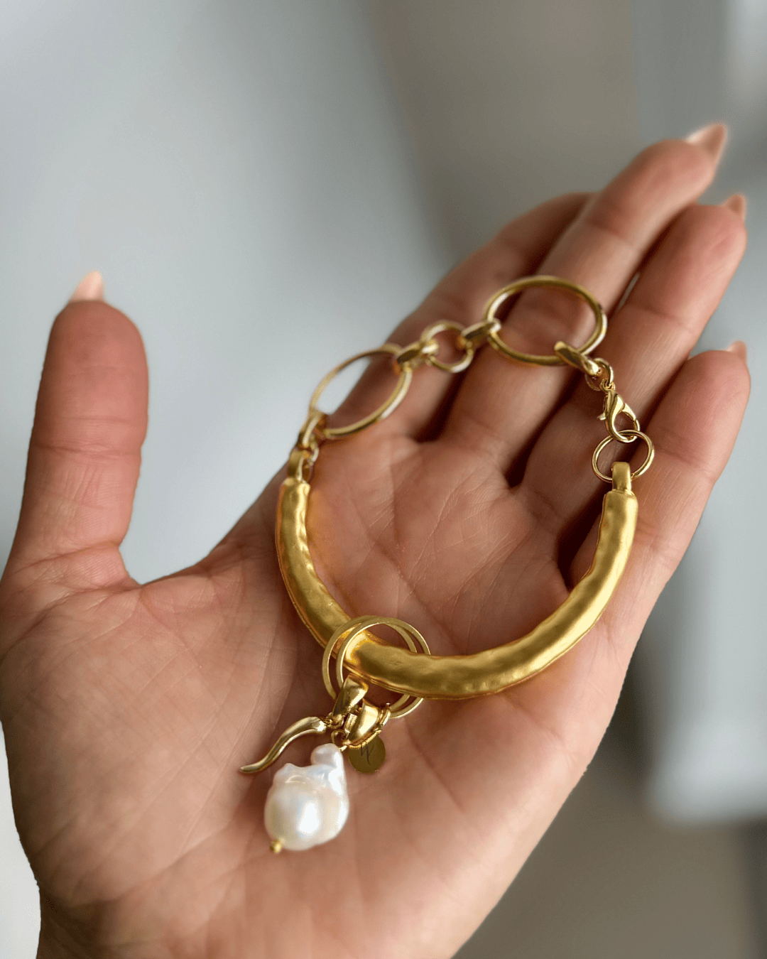 Gold bracelet with a pearl charm held in a hand against a neutral background