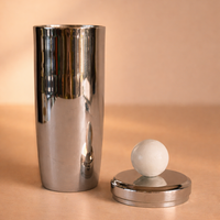 Metallic cylindrical container with a spherical object on a beige background