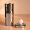 Metallic cylindrical container with a spherical object on a beige background
