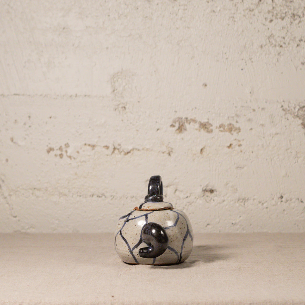 Small ceramic teapot with black and blue patterns on a textured beige background