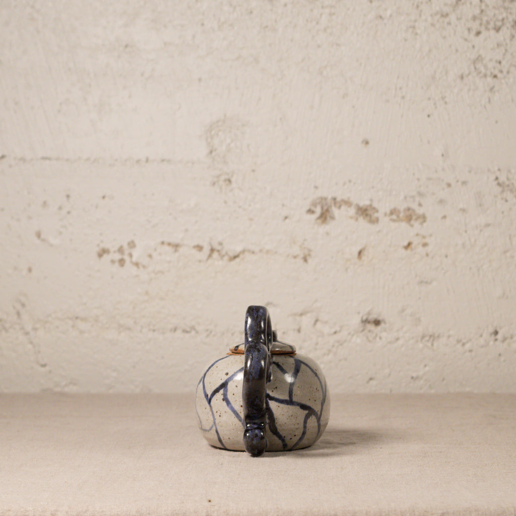 Small ceramic teapot with a indigo handle on a textured beige surface