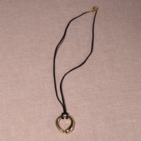 A gold heart-shaped pendant necklace on a black cord, displayed on a textured beige linen background.
