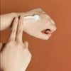 Hand applying cream to another hand against a brown background
