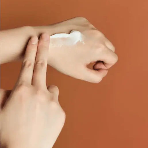 Hand applying cream to another hand against a brown background