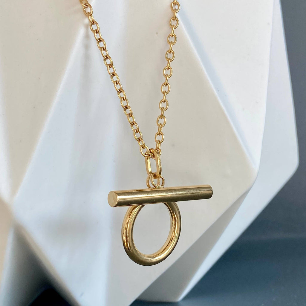 Gold necklace with a unique pendant on a white geometric background