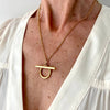 Gold necklace with a unique pendant worn by a person in a white outfit.