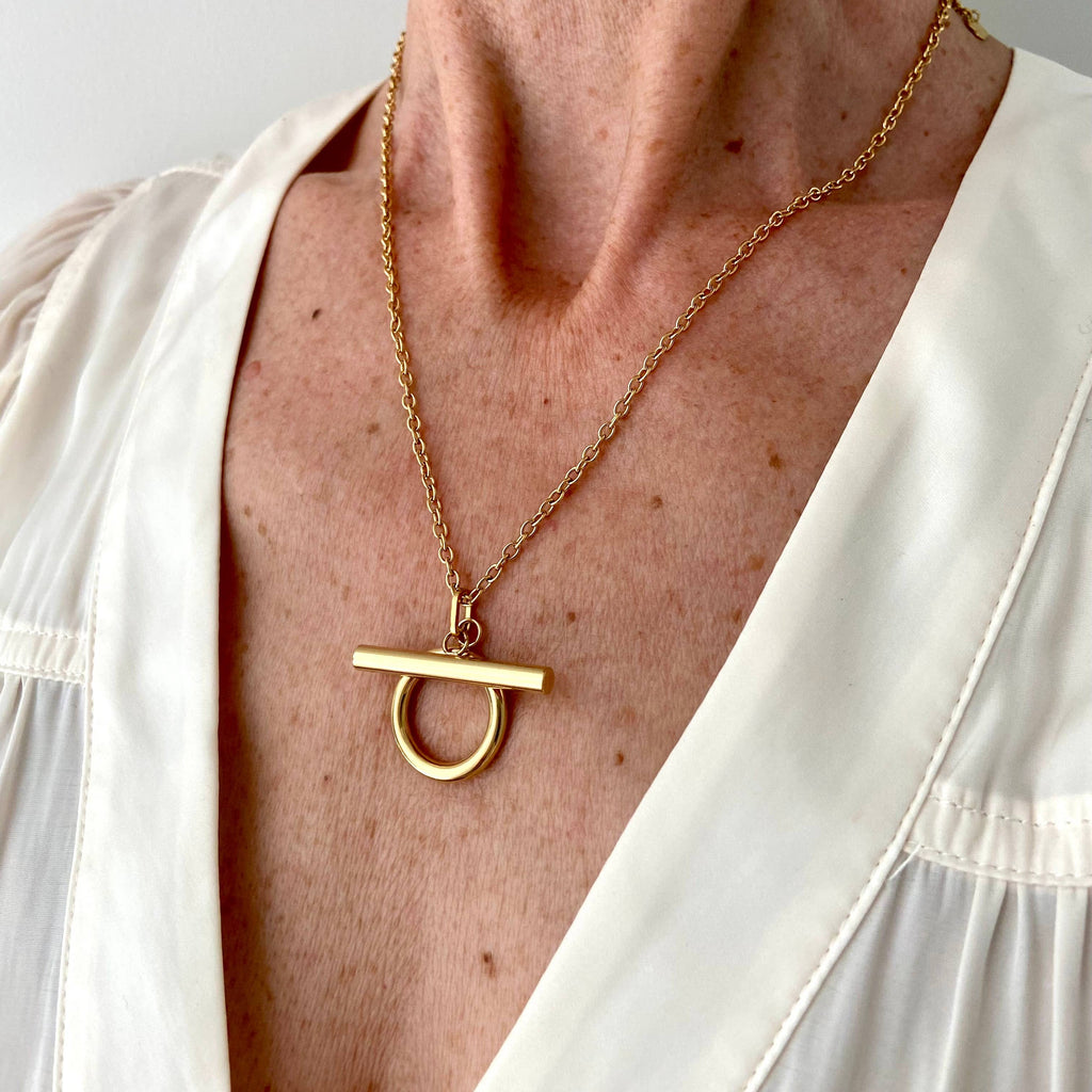 Gold necklace with a unique pendant worn by a person in a white outfit.