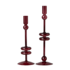 Two dark red glass candlesticks with unique stacked circular designs on their stems, set against a plain white background.