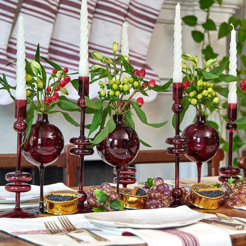 Decorative table setting with red glass candle holders, greenery, and white candles.