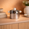 Silver ice bucket with spherical handles on a wooden surface with decorative elements.