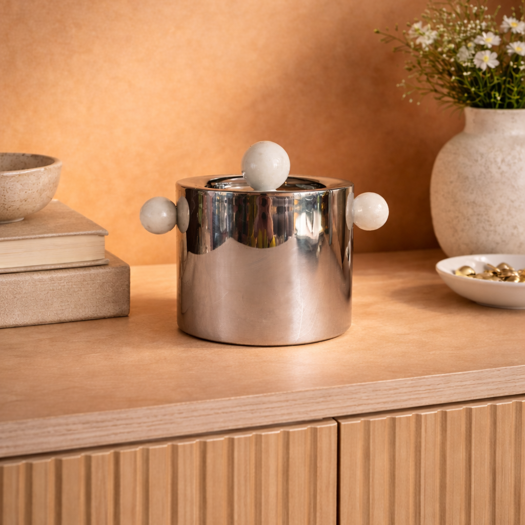 Silver ice bucket with spherical handles on a wooden surface with decorative elements.