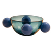 A translucent blue-green glass bowl with four rounded protruding spheres, photographed on a warm beige studio background with a soft shadow.