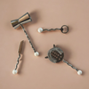 Set of cocktail tools including a jigger, strainer, and muddler on a beige background