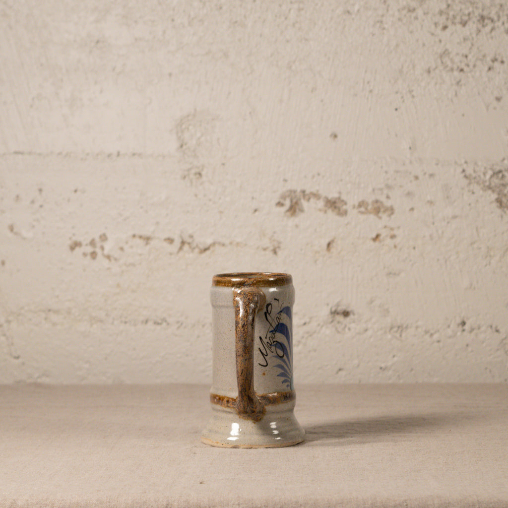 Small ceramic cup with decorative handle on a textured surface