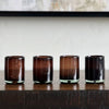 Four dark glass tumblers on a wooden surface with a neutral background