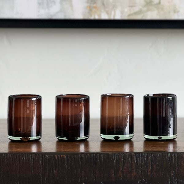 Four dark glass tumblers on a wooden surface with a neutral background