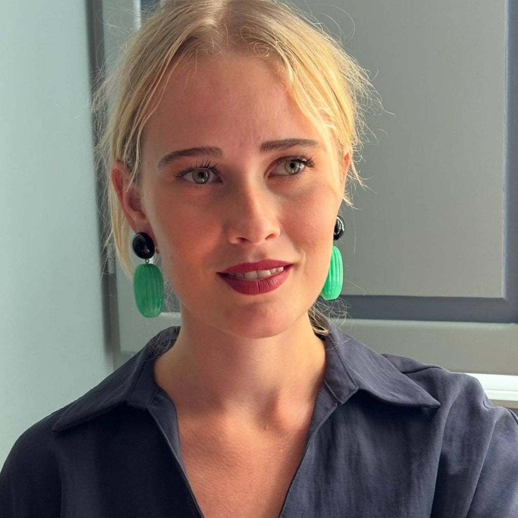 Woman wearing green earrings and a dark shirt indoors.