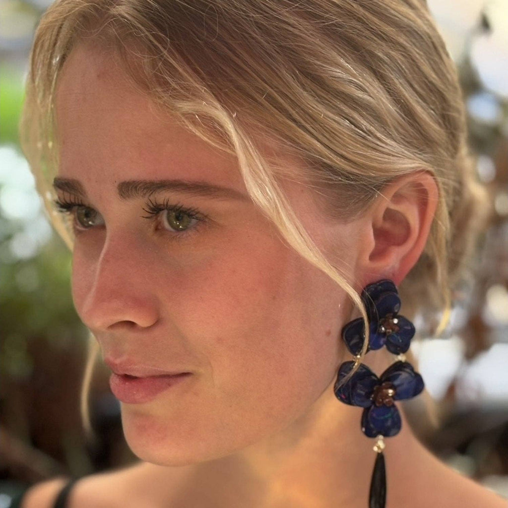 Close-up of a woman wearing blue floral earrings with a blurred natural background