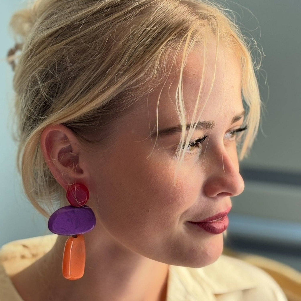 Close-up of a person wearing colorful earrings with a blurred background