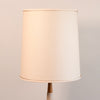 A classic drum lampshade in a warm cream or off-white linen fabric, shown on a matching table lamp against a neutral light beige background.